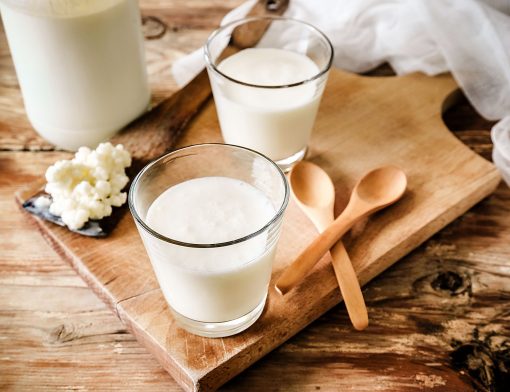 intolerância à lactose: na imagem diversos copos de leite em tábua de madeira, que acompanha colheres.