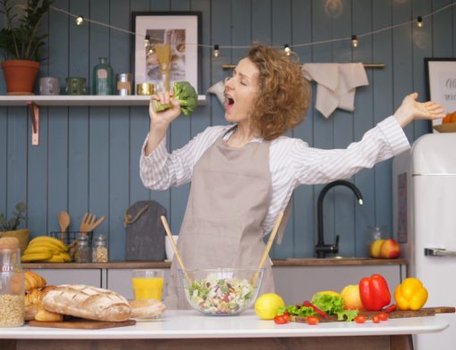 mulher preparando comida, segurando brócolis como se fosse um microfone