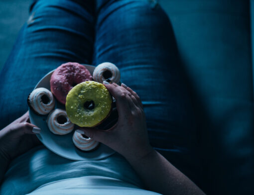 Pessoal deitada em um sofá com um prato com doces coloridos em forma de rosquinhas.