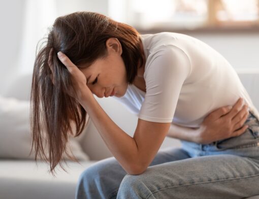Pessoa sentada com expressão de desconforto abdominal, com uma das mãos na linha da cintura e a outra na região da testa.