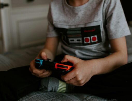 Uma criança sentada, com uma estampa de um controle retrô de videogame, segurando um controle de videogame. 