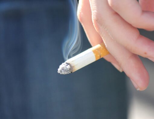 Um fumante segura um cigarro aceso entre os dedos de uma das mãos
