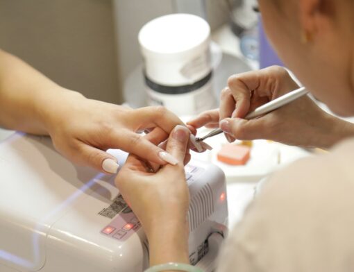 Profissional de estética efetuando procedimentos nas unhas de uma clientes em um estúdio com equipamentos adequados
