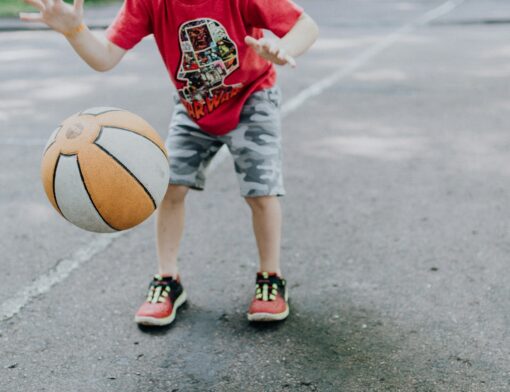 Uma criança em um local de prática de atividade física e esportes com uma bola de basquete.