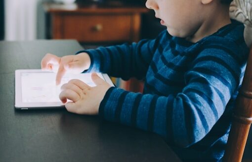 Criança sentada à mesa interagindo com um dispositivo do tipo tablet.
