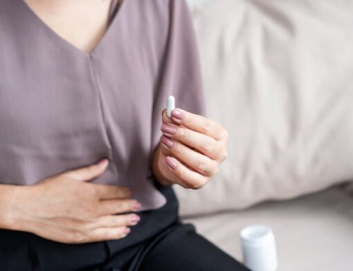 Uma pessoa com a mão na região do abdômen devido ao desconforto gástrico, preparando-se para tomar medicamento