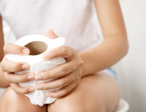 Uma pessoa sentada no vaso sanitário com preocupações devido a cor das fezes, aparenta desconforto. Entender os sinais do corpo é fundamental.